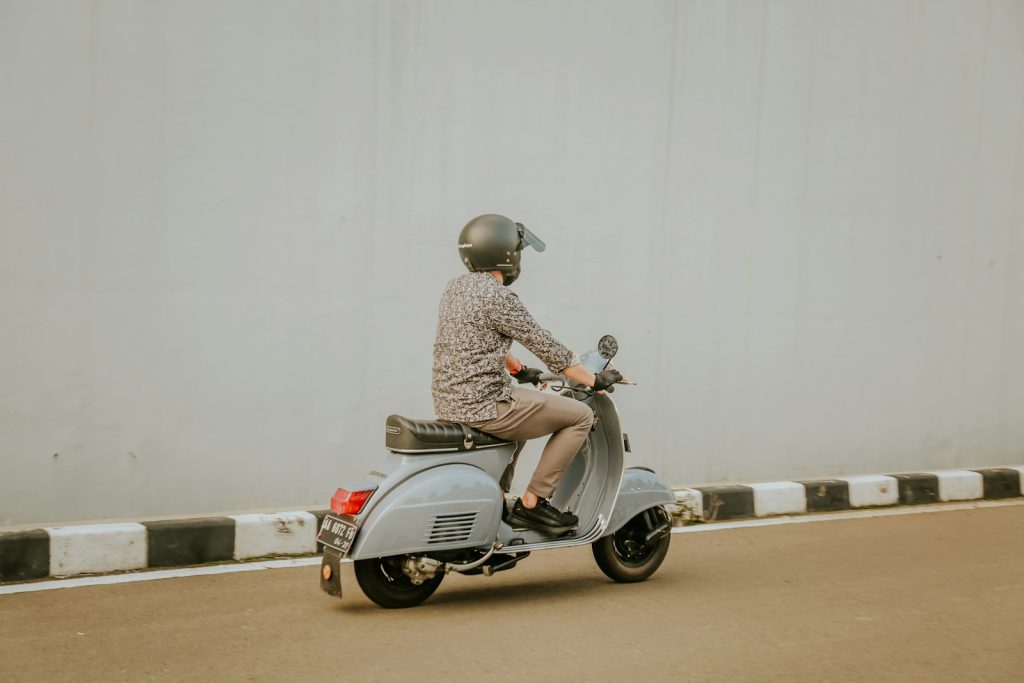 man in brown and white checkered dress shirt riding on gray motor scooter